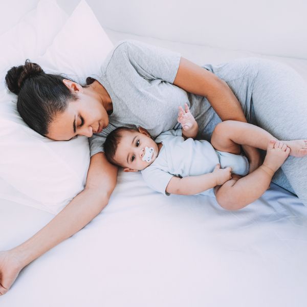 Mother resting in bed with her baby while coping with postpartum night sweats and disrupted sleep